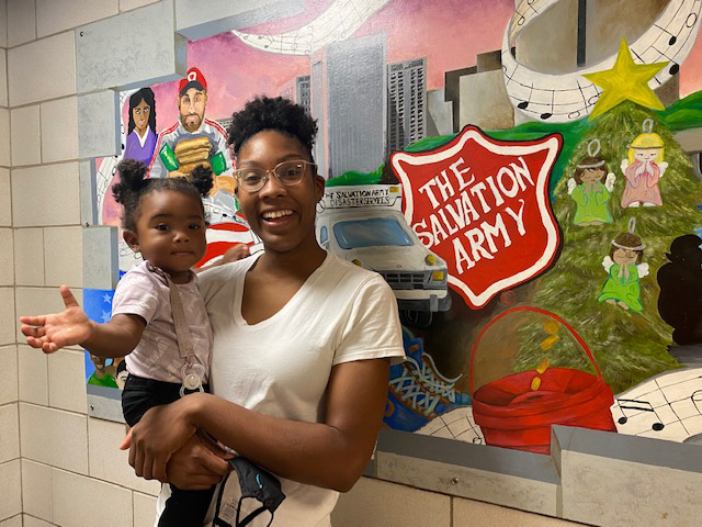 Tyshell - parent holding child in front of Salvation Army bulletin board.